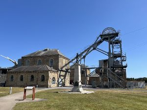 Woodhorn Museum, site of the Woodhorn Colliery showing one of the winding houses, headframe and headgear. Opened in 1894, the colliery was a working mine for 80 years, at its peak producing 600,000 tonnes of coal each year. In the foreground Ashington Miners' Memorial commemorating the victims of the Woodhorn Colliery disaster on 3 August 1916.