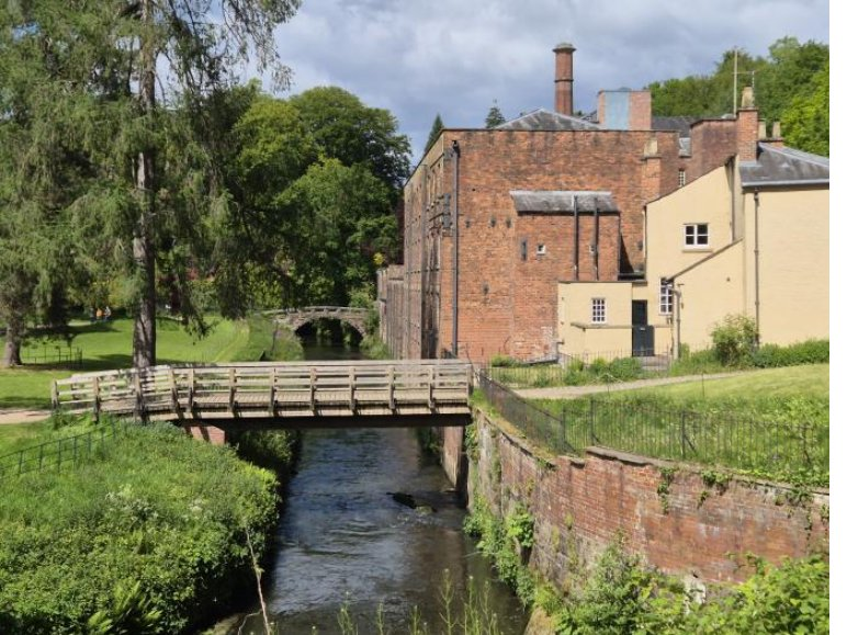 The mill race running past the brick buildings of Quarry Bank Mill, with a footbridge over it