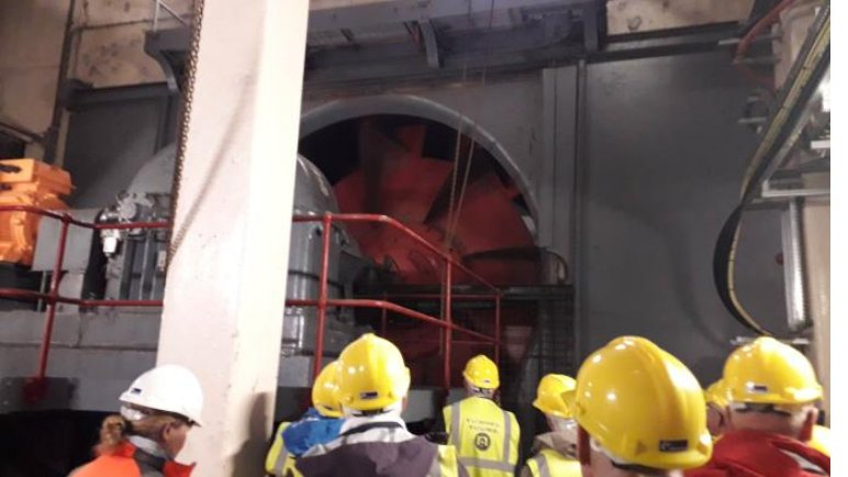 Members in yellow hard hats in front of a huge exhaust fan in the Mersey tunnel ventilation building